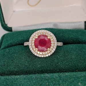 May include: A red ruby ring with a double halo of diamonds set in yellow gold.