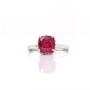 May include: A silver ring with a large, square-shaped ruby gemstone set in a halo of smaller diamonds.