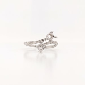 May include: A silver-toned ring with two settings, each designed to hold a gemstone. The band is adorned with small, sparkling stones. The ring has a unique, asymmetrical design, perfect for a custom jewelry piece.