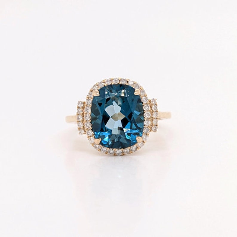 May include: A gold ring featuring a large, cushion-cut blue topaz gemstone encircled by a halo of smaller diamonds.