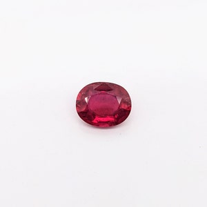 May include: A deep red oval gemstone with facets.
