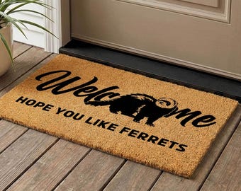 May include: A rectangular doormat made of natural fibers. The mat features the word "Welcome" in a cursive font, with a black ferret silhouette and the phrase "HOPE YOU LIKE FERRETS" in a bold, sans-serif font.