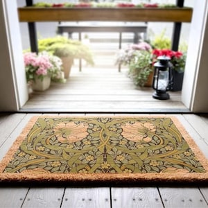 a decorative mat with a floral pattern on a wooden floor, with a view of a wooden deck and potted plants through an open doorway.
