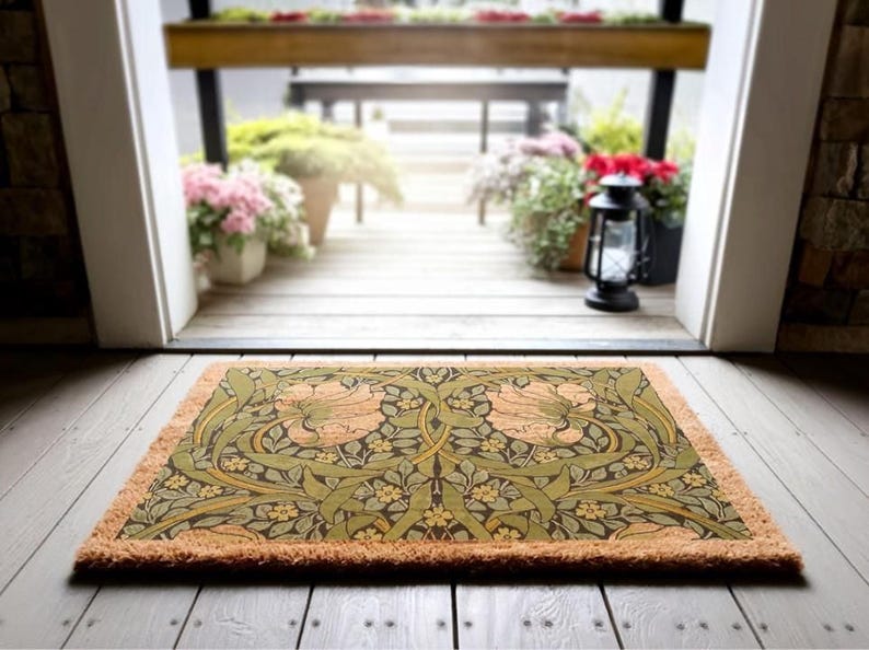 a decorative mat with a floral pattern on a wooden floor, with a view of a wooden deck and potted plants through an open doorway.