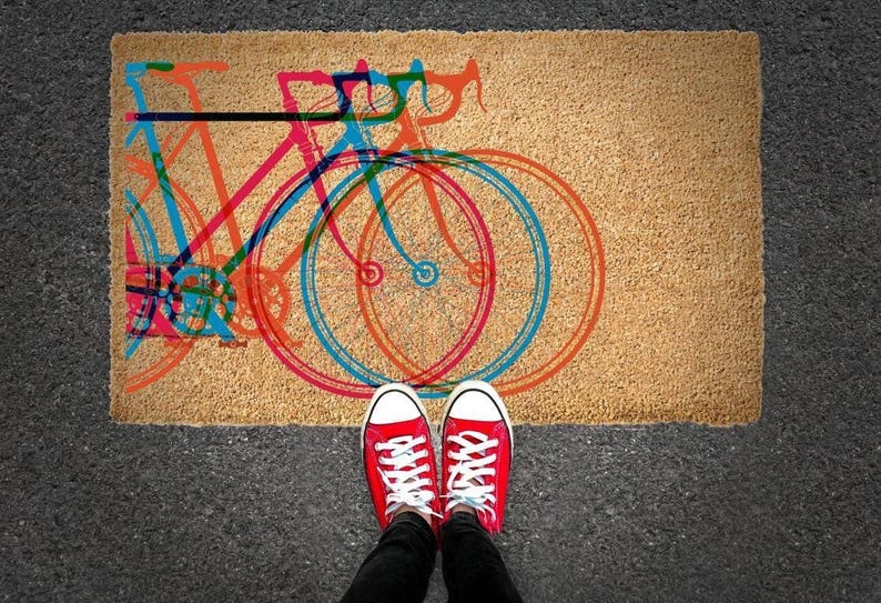 A pair of red and white sneakers stands on a doormat with a colorful bicycle design.