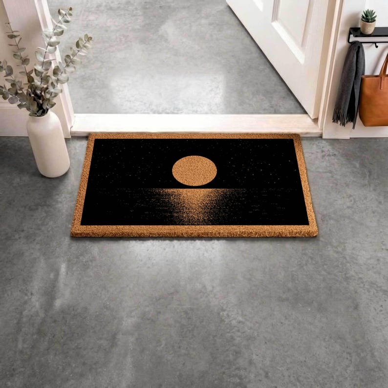 a black and gold door mat with a circular design on it, placed on a gray floor next to a white door.
