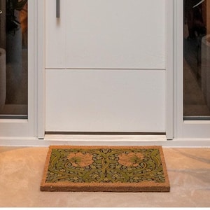 a white door with a decorative mat placed in front of it, flanked by two potted plants on either side.