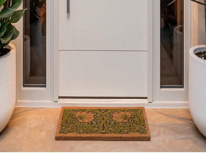 a white door with a decorative mat placed in front of it, flanked by two potted plants on either side.