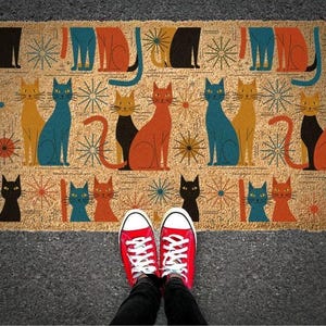 A pair of red Converse sneakers stands on a colorful, patterned doormat featuring various cat illustrations.