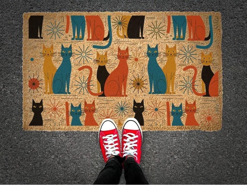 A pair of red Converse sneakers stands on a colorful, patterned doormat featuring various cat illustrations.