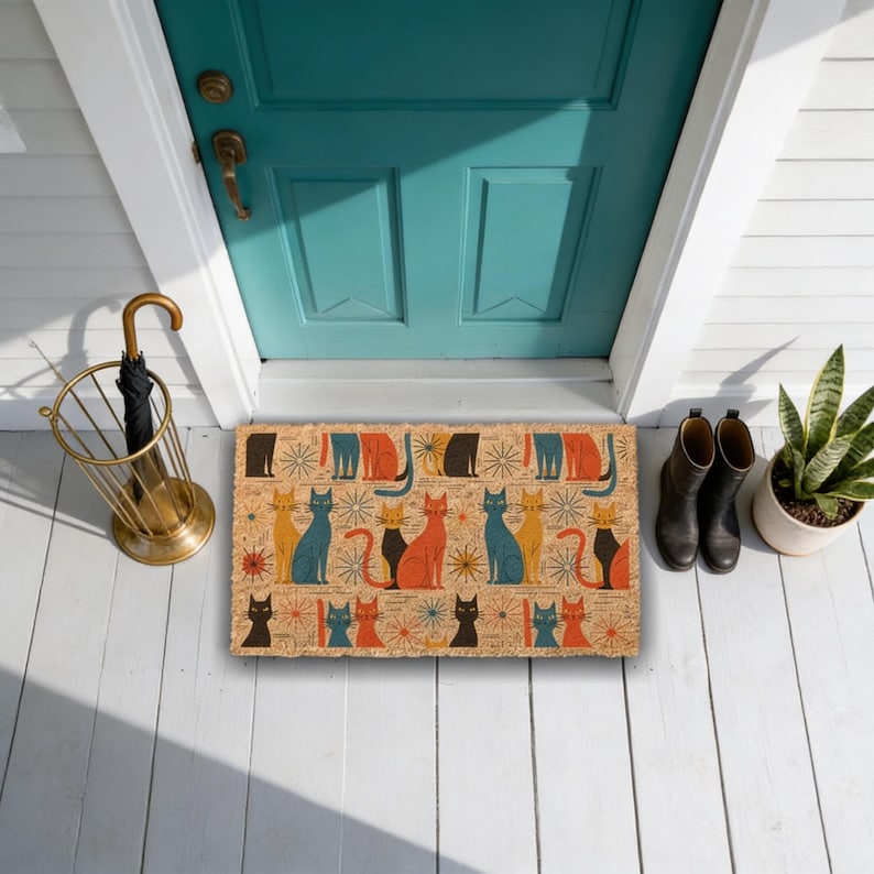 a colorful, patterned door mat with a variety of cats on it, placed on a white wooden porch. Next to the mat, there is a gold umbrella stand and a pair of black boots. A potted plant is also present in the scene.