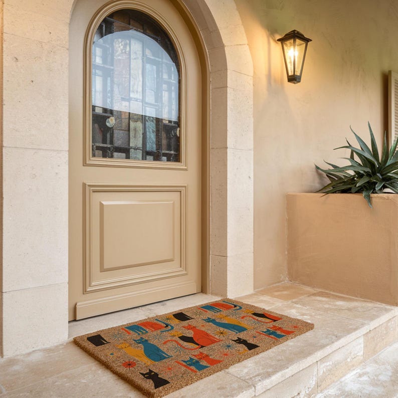 a beige door with a window, a light fixture above it, and a colorful welcome mat on the steps leading up to the door.