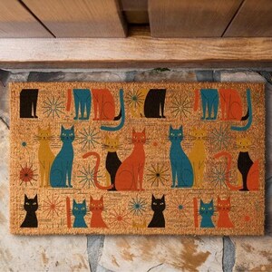 A colorful, patterned door mat with various cat illustrations on it, placed on a stone surface.
