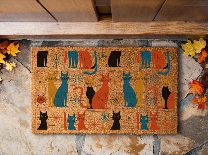 A colorful, patterned door mat with various cat illustrations on it, placed on a stone surface.