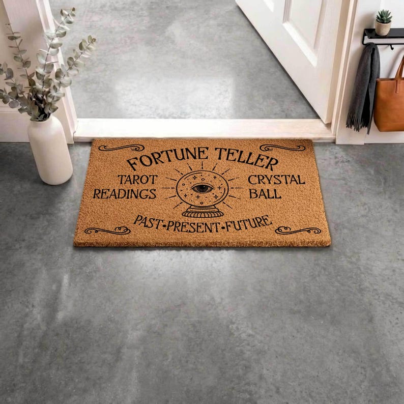 May include: A rectangular doormat made of natural brown coir fiber. The mat features black text that reads "Fortune Teller" above a crystal ball graphic, with "Tarot Readings" and "Crystal Ball" on either side. The words "Past-Present-Future" are below the crystal ball.