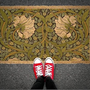 A pair of red sneakers stands on a decorative rug with a floral pattern, positioned on a gray pavement.