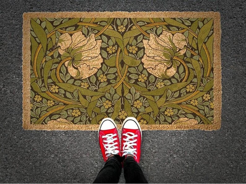 A pair of red sneakers stands on a decorative rug with a floral pattern, positioned on a gray pavement.