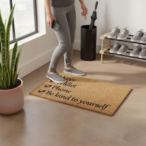 A person standing in a room with a shoe rack, a potted plant, and a doormat with a message on it.