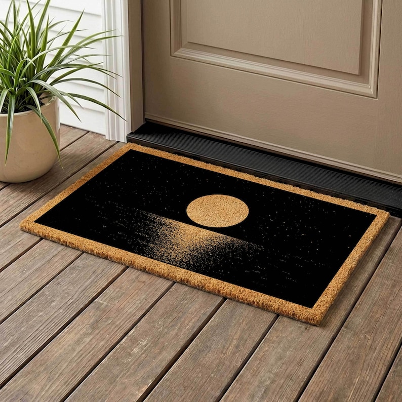 A black and gold door mat with a design depicting a sunset or sunrise on a wooden floor next to a door.