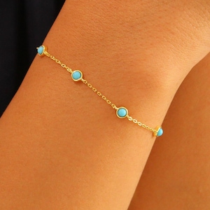 May include: A delicate gold chain bracelet with small turquoise blue stones. The bracelet is on a person's wrist.