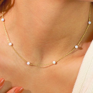 May include: A delicate gold chain necklace with small white opal beads. The necklace is simple and elegant, perfect for everyday wear.