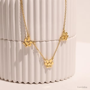 Puede incluir: Collar de oro con tres colgantes con forma de huella de pata. Cada colgante tiene un nombre grabado: Anna, Ruby y Luna.