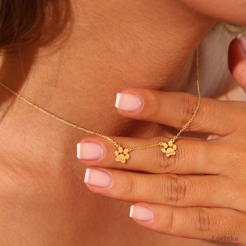 Puede incluir: Un collar de cadena dorada con dos dijes en forma de huella de pata. Los dijes est&aacute;n grabados con las palabras "Luna" y "Ruby".