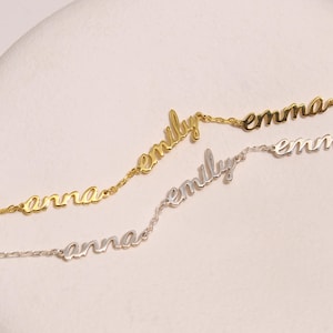 May include: Three delicate name necklaces in gold and silver. The names "Anna", "Emily", and "Emma" are displayed in a cursive font. The necklaces are on a white surface.