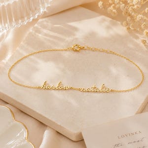K&ouml;nnte beinhalten: Ein goldfarbenes Kettenarmband mit den zwei Namen harlow und natalie in kursiver Schrift. Das Armband verf&uuml;gt &uuml;ber einen kleinen runden Verschluss und ein verstellbares Kettenglied-Element, das ein zartes und poliertes Metallfinish aufweist.