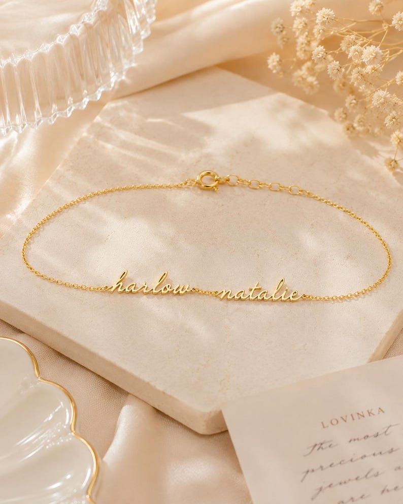 K&ouml;nnte beinhalten: Ein goldfarbenes Kettenarmband mit den zwei Namen harlow und natalie in kursiver Schrift. Das Armband verf&uuml;gt &uuml;ber einen kleinen runden Verschluss und ein verstellbares Kettenglied-Element, das ein zartes und poliertes Metallfinish aufweist.