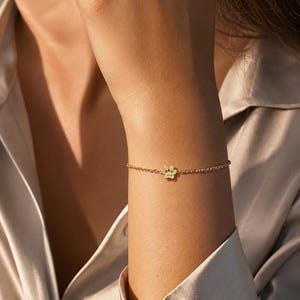 May include: A gold-toned chain bracelet featuring a small, central paw print charm. The charm is engraved with the name Jack. The bracelet is constructed with a delicate, fine link chain that secures around the wrist with a simple clasp mechanism.