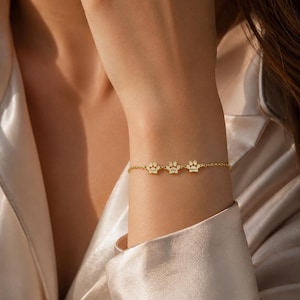 May include: A gold-toned chain bracelet featuring three small, evenly spaced paw print charms. Each charm is engraved with a name. The bracelet is secured with a delicate link chain. The text LOVINKA with a heart icon is visible in the corner.