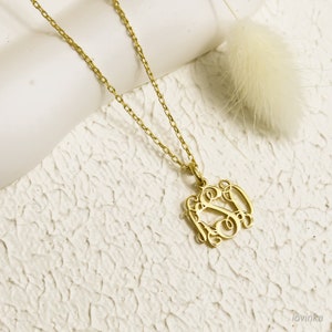 May include: A gold chain necklace with a gold pendant featuring a monogram design. The pendant is a delicate, intricate design of three letters intertwined.