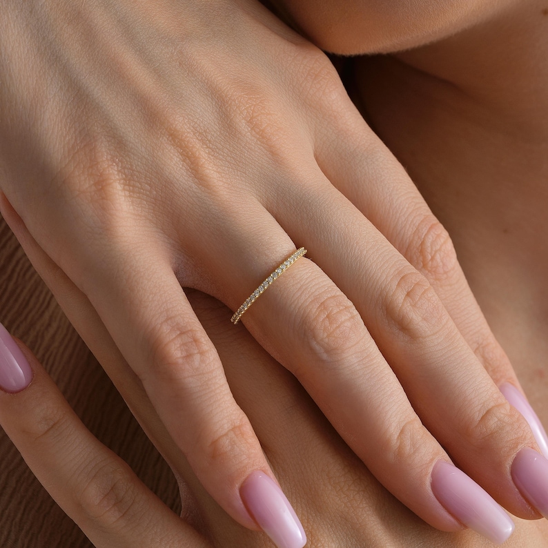 A woman wearing a 14K gold eternity ring with micro pave diamonds, thin delicate band for stacking, elegant minimalist engagement or wedding ring by Lovinka.
