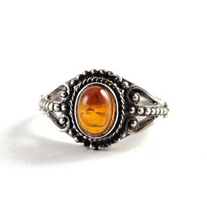 May include: A silver ring with an oval amber gemstone set in a decorative filigree design.