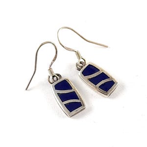 May include: A pair of silver earrings with a rectangular design. Each earring features a dark blue inlay with curved silver lines. The earrings have a hook closure and are displayed against a white background.