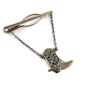 May include: Silver tie tack with a chain and a detailed cowboy boot charm.