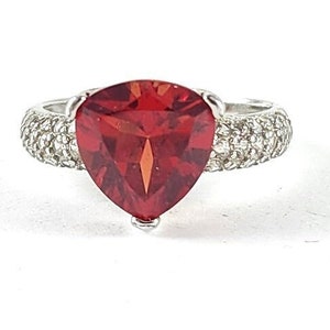 May include: A silver ring with a large, red, triangular gemstone surrounded by smaller, white gemstones.