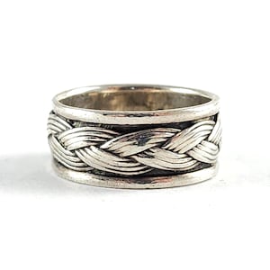 May include: A silver ring with a braided design around the center. The ring has a band on the top and bottom, with the braided section in between. The ring is set against a white background.