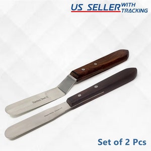 May include: Set of two stainless steel offset spatulas with wooden handles. The spatulas are marked "Stainless Steel CE".
