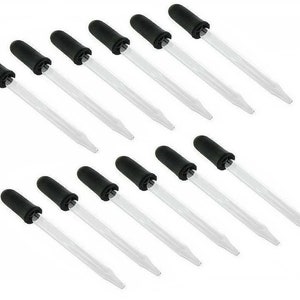 May include: A collection of twelve clear glass pipettes with black rubber bulbs. The pipettes are arranged in two rows of six, against a white background. Each pipette has a long, slender, transparent tube for precise liquid transfer.