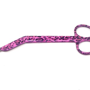May include: Pink surgical scissors with a leopard print design. The scissors have a curved handle and sharp blades.