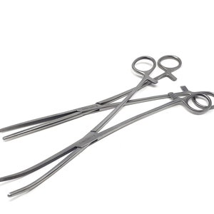 Puede incluir: Dos hemostáticos de acero inoxidable, uno recto y otro curvo, con el texto "German Stainless CE" en los mangos.