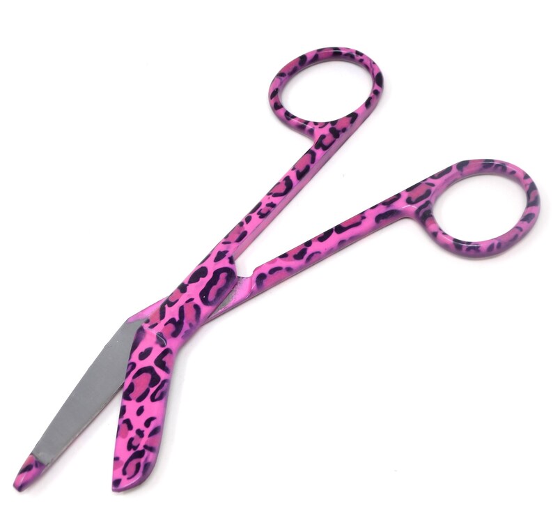 May include: Pink bandage scissors with a leopard print design. The scissors have a curved blade and a sharp point.