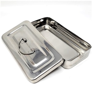 Puede incluir: Una caja rectangular de acero inoxidable con tapa abatible y asa. La caja está vacía y tiene un acabado brillante.