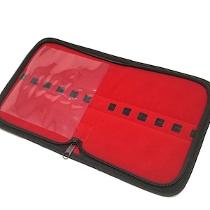 May include: A black zippered case with a red velvet interior and a clear plastic window. The case has multiple slots for holding small items.