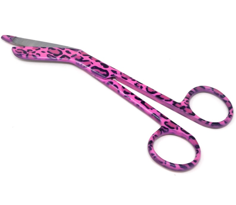 May include: Pink bandage scissors with a leopard print design. The scissors have a curved blade and a ring handle.