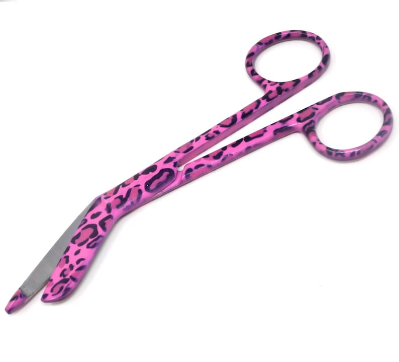 May include: Pink bandage scissors with a leopard print design. The scissors have a curved blade and are made of stainless steel.