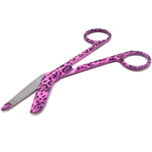 May include: Pink surgical scissors with a leopard print design. The scissors have a curved blade and are made of stainless steel.