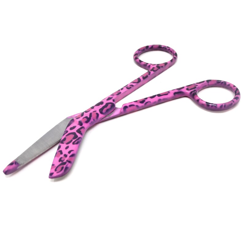 May include: Pink surgical scissors with a leopard print design. The scissors have a curved blade and are made of stainless steel.